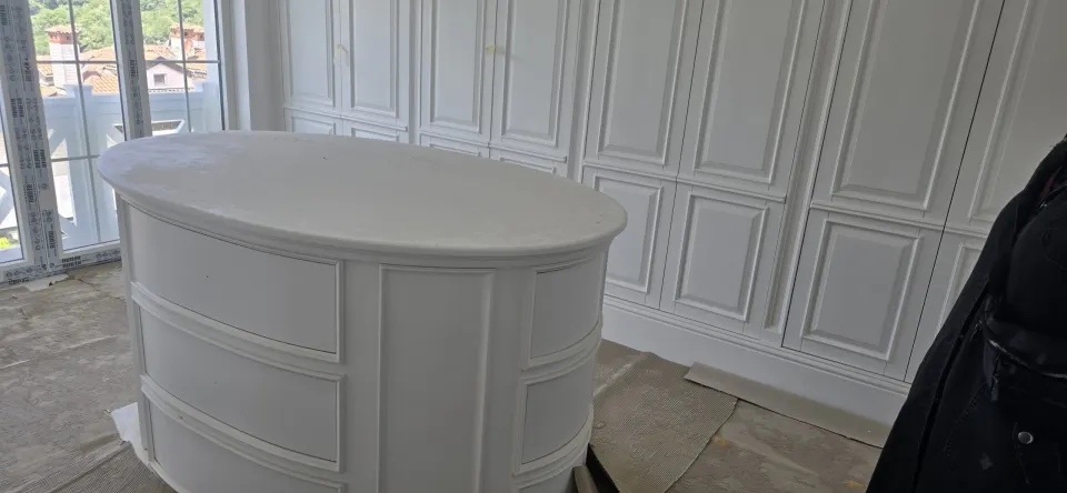 Villanın giyinme odasında oval beyaz çekmeceli ada ve duvar boyu panel kapaklı dolaplar